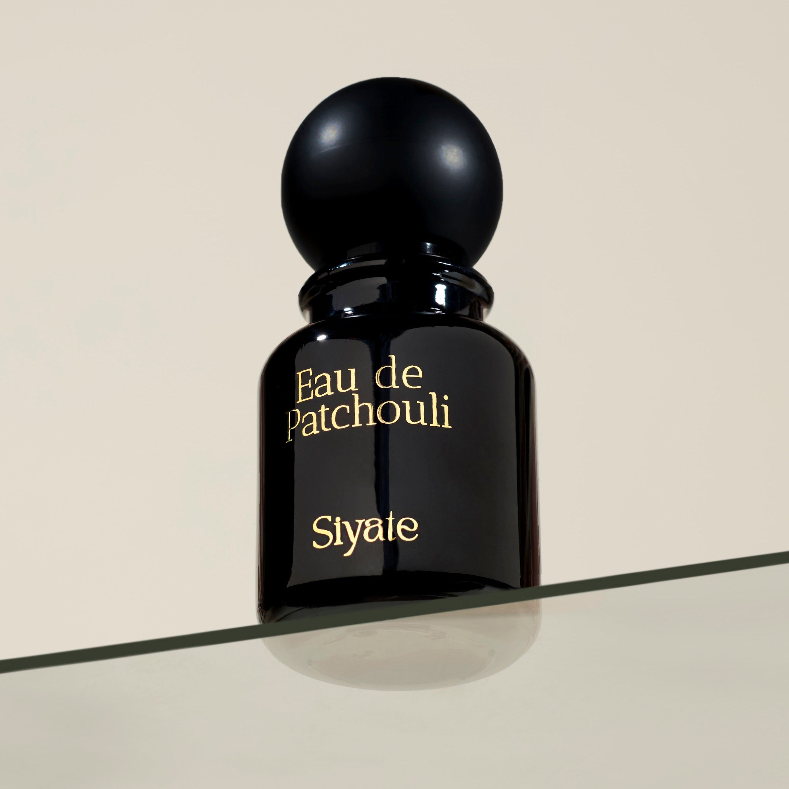 Black perfume bottle labeled 'Eau de Patchouli' by Slytte on a beige background