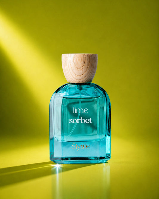 A bottle of Syate Lime Sorbet fragrance with bright turquoise-blue liquid, a light wood cap, and white lettering, set against a vibrant yellow-green background with dramatic diagonal light rays.