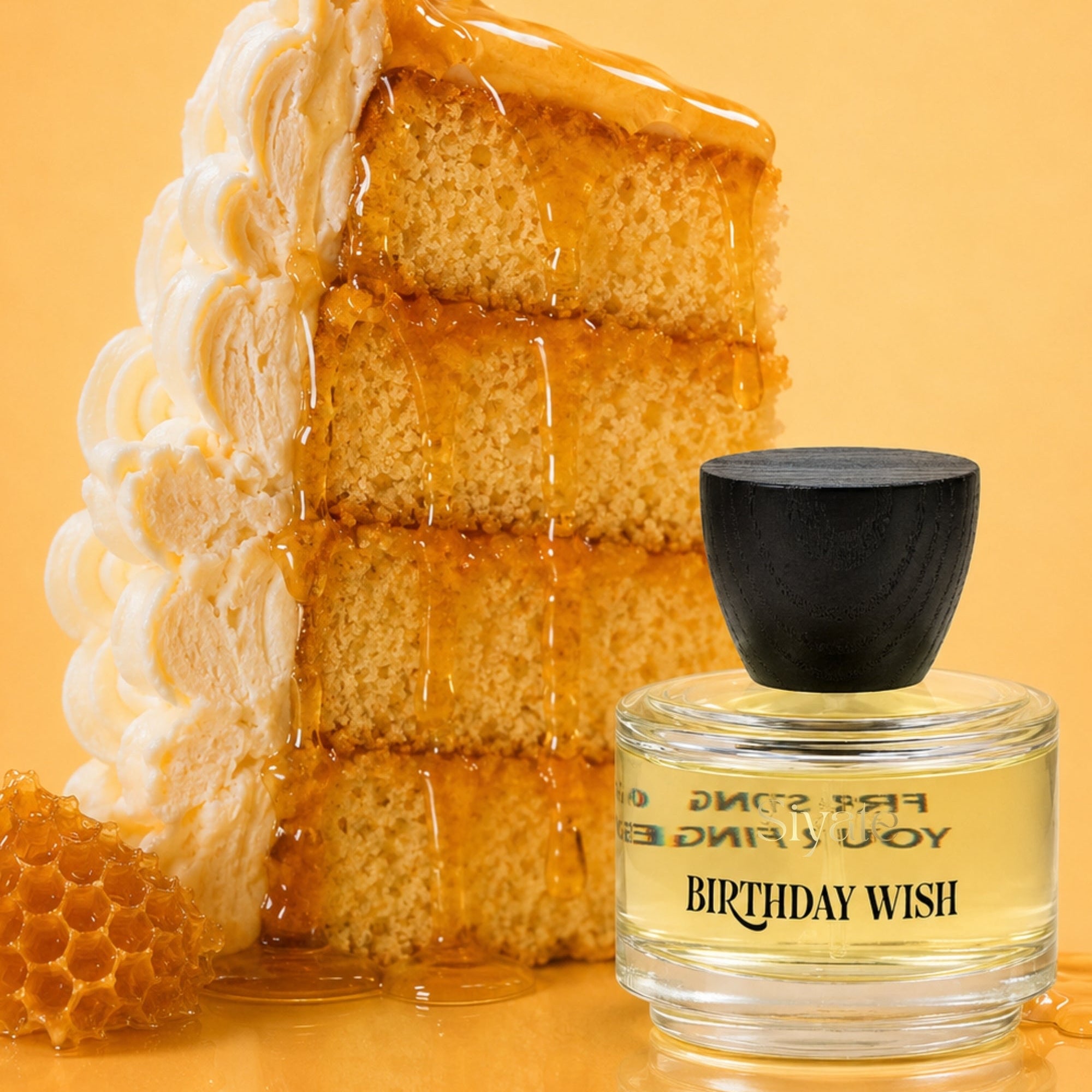 A perfume bottle labeled 'BIRTHDAY WISH' with a black cap, placed in front of a large slice of layered cake dripping with honey, on a warm yellow background.