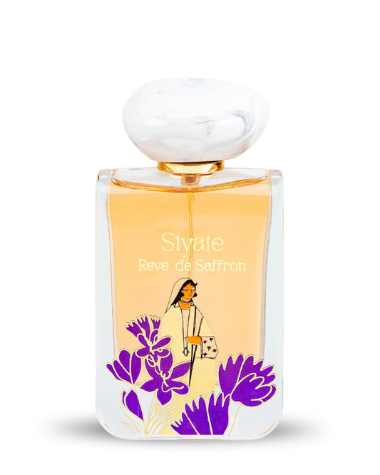 A rectangular glass perfume bottle with a rounded white cap, filled with pale golden-yellow fragrance. The front label reads 'Siyale Reve de Saffron' and features purple saffron flowers and a small illustrated woman.
