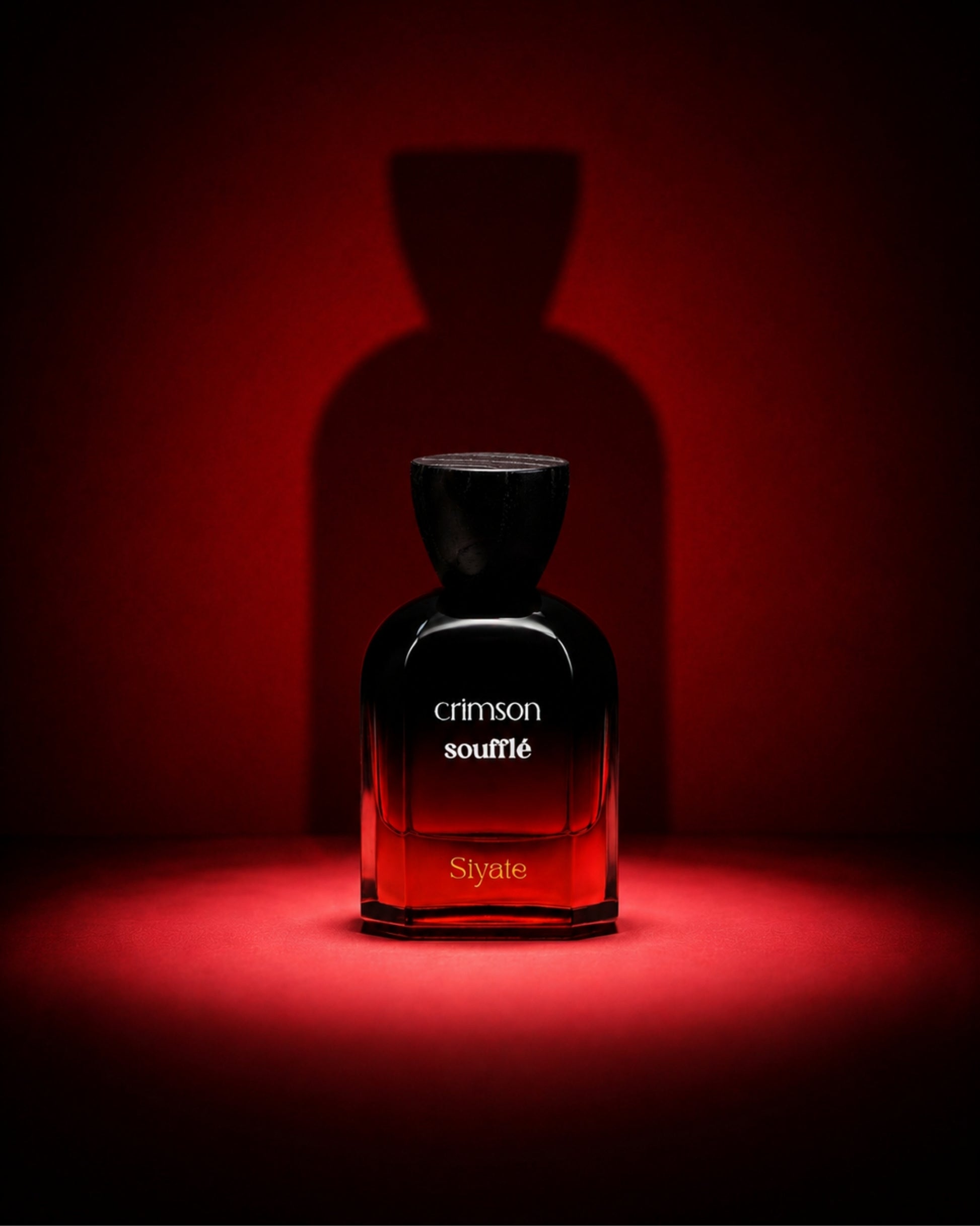 A dark glass perfume bottle labeled 'crimson souplé' and 'Siyate' stands centered on a red-lit surface against a matching red background, with a large shadow behind it.