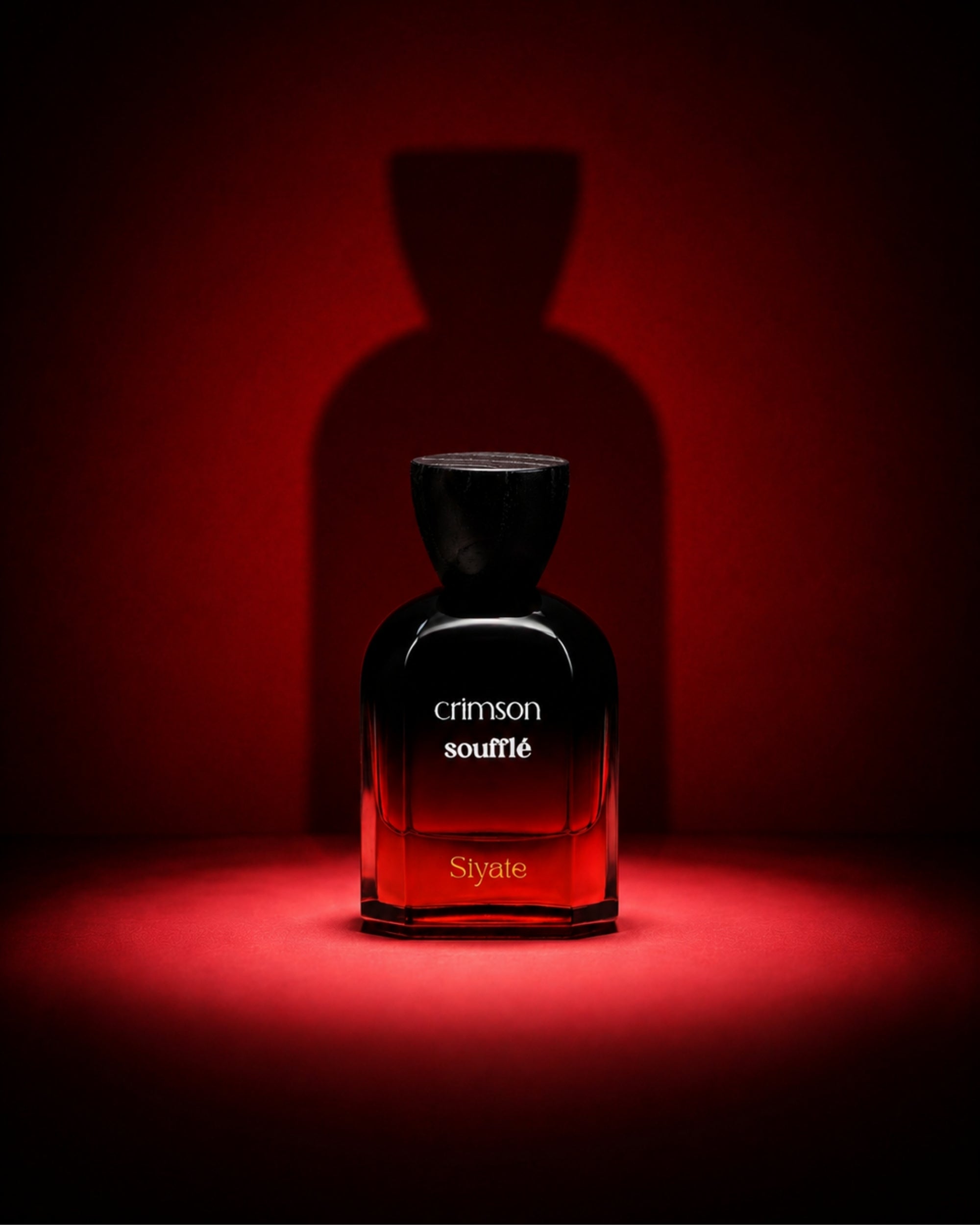 A dark glass perfume bottle labeled 'crimson souplé' and 'Siyate' stands centered on a red-lit surface against a matching red background, with a large shadow behind it.
