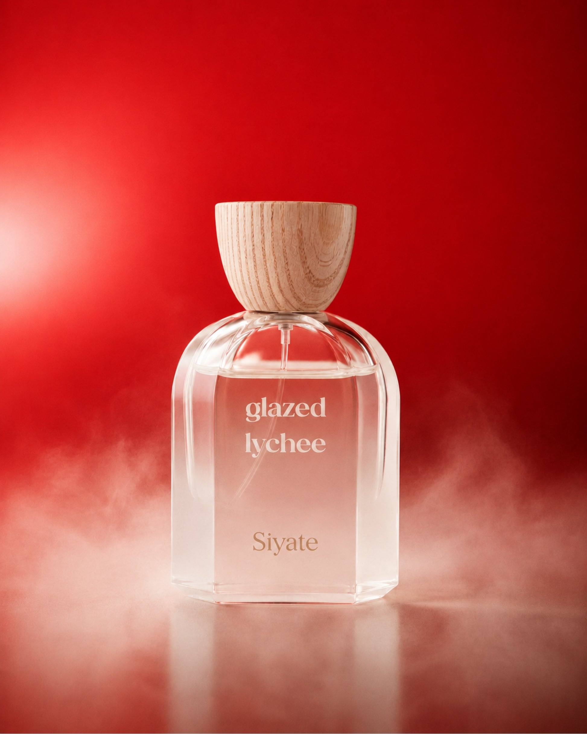 A clear glass perfume bottle labelled 'glazed lychee' and has the 'Siyate' logo with a light wood cap, centered on a red background with soft mist around the base.