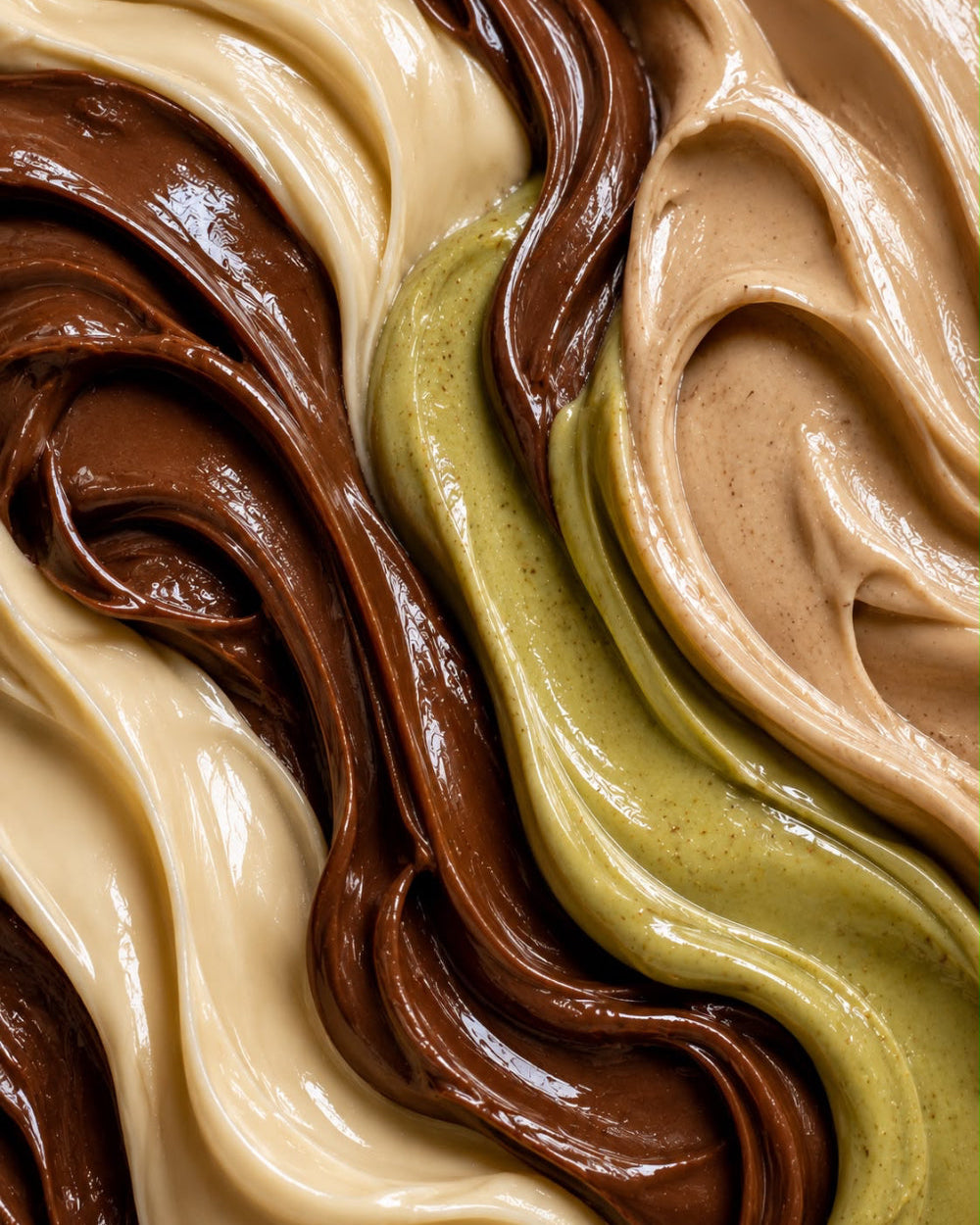 Close-up of swirled whipped cream or frosting in four colors: light beige, dark brown, olive green, and tan.